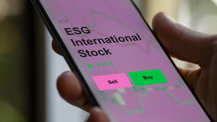 An investor's analizing the esg international stock etf fund on a screen. A phone shows the prices of ESG International Stock