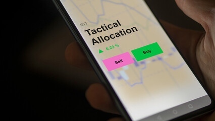 An investor's analizing the tactical allocation etf fund on a screen. A phone shows the prices of Tactical Allocation