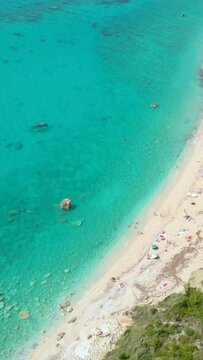 DRONE: Carefree tourists enjoying their summer holidays on the remote sandy beach in Greece. Scenic aerial view of the untouched shoreline of a hidden isle in beautiful turquoise Mediterranean sea.