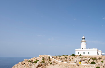 Fototapeta na wymiar a white lighthouse on a cliff with the sea in the background on a clear summer day, Cavalleria Lighthouse, Fornells, Menorca, Balearic Islands, Spain, copy space
