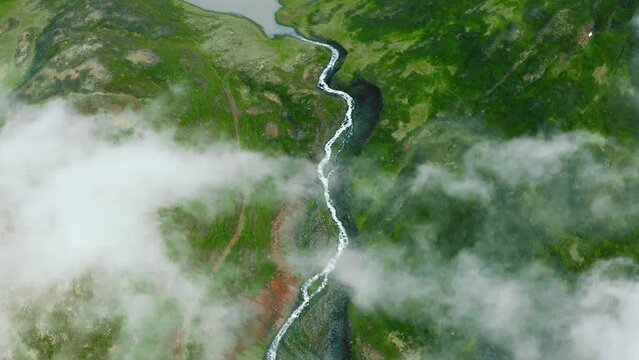 Aerial top view of nordic landscape, flyover green valley beautiful formations, flight through rainy clouds. Cinematic drone shot of amazing north fjord small lake and winding river in Iceland