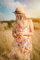 woman in dress and hat walking in a wheat field in summer