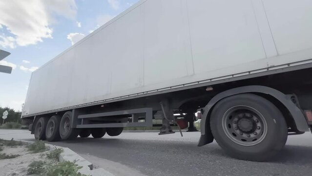 Semi-trailer truck leaves the territory of the logistics park with warehouses after unloading and loading on the ramp. Side view. Low wide angle shot