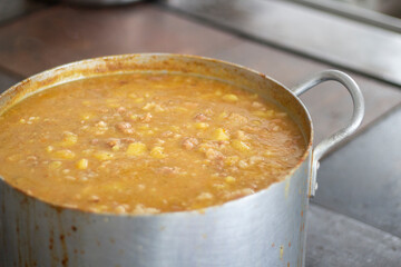 Soup in saucepan. Large container with pea soup in kitchen. Stainless steel cookware. Steel tank with food in dining room.