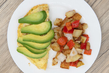Overhead view of standard American breakfast consisting of chicken omelet with sliced avocado and seasoned potatoes will ensure that the belly will be full