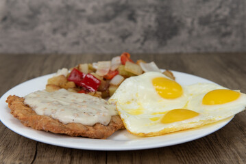 Standard American breakfast consisting of chicken fried steak, covered in gravy, fried eggs, and seasoned potatoes will ensure that the belly will be full