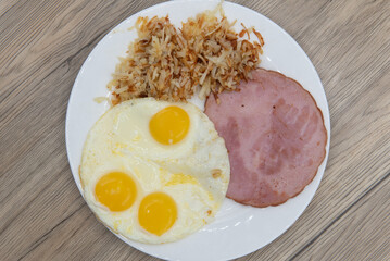 Overhead view of standard American breakfast consisting of ham, fried eggs, and hash browns will ensure that the belly will be full