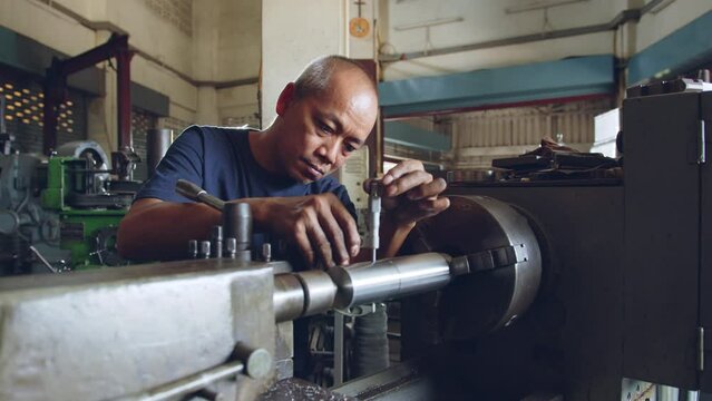 Technician asia worker using vernier caliper measure detail of workpiece for checking size in workshop lathe machine factory