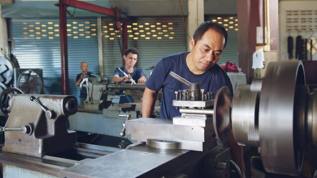 Technician asia worker using turning lathe machine for metalworking in workshop factory