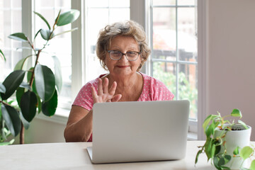 Senior woman sitting at desk talking on video chat using laptop computer