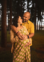 pregnant latin couple embracing watching each other in pine forest