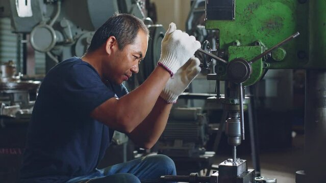 Technician worker using drilling machine for metalworking in workshop factory