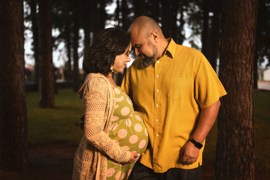 pregnant latin couple embracing watching each other in pine forest