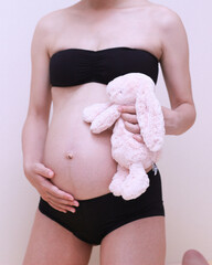 妊婦の身体とお腹の中の赤ちゃんとうさぎのぬいぐるみ - obrazy, fototapety, plakaty