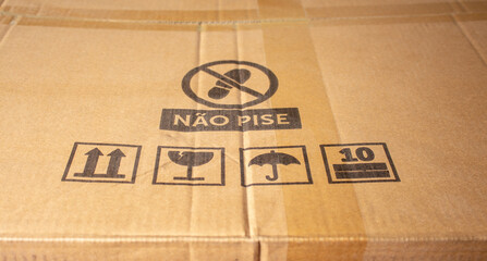 Cardboard box with care symbols, and description "don't step on" in Portuguese.