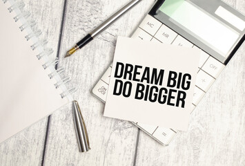 Text Think Big Do Bigger on paper card and calculator on wooden background