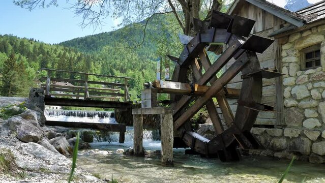 Old wooden water mill with a small waterfall in the background and stone house. Colorful background with hills and wood of Slovenia. 4k 50 fps shot
