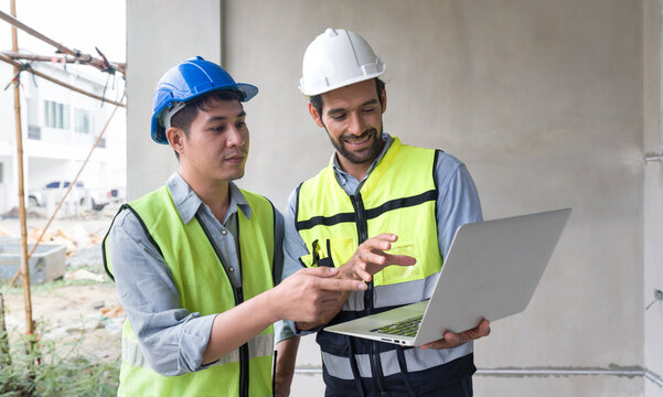Young engineer with laptop computer explain to foreman about a floor plan. Both wear  construction helmet and safety vest. Work environment at the construction site of housing projects.