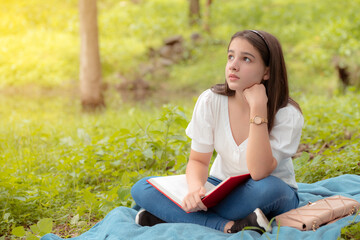 young girl with high hopes sitting in the forest reading a book on a blue blanket