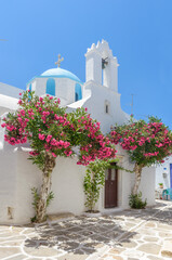 Traditional Cycladitic alley with a narrow street and a whitewashed church with a blue dome in Parikia, Paros island, Greece.