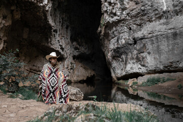 A mexican bandit wearing a poncho is waiting alone hiding in the mountains