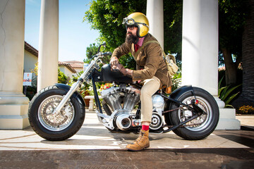 A man with a beard on a motorcycle wearing a gold helmet