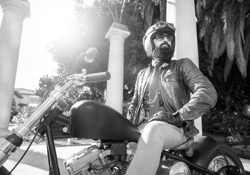 Black and White image of a man with a beard on a motorcycle wearing a gold helmet