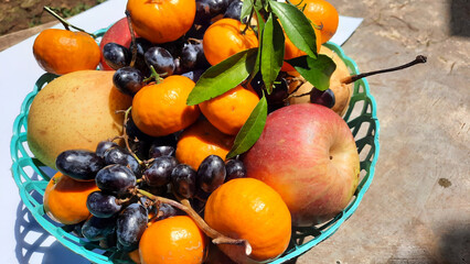 Close up of apples, pears, grapes and oranges in green basket on exposed cement background
