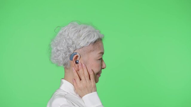 補聴器をつけるシニア女性　クロマキー合成用グリーンバック