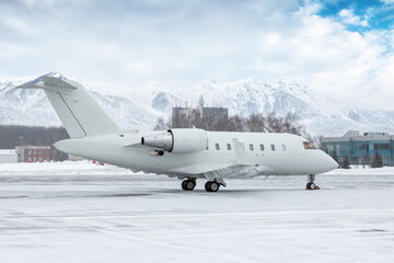 Fototapeta na wymiar White luxury executive airplane on the winter airport apron on the background of high scenic mountains