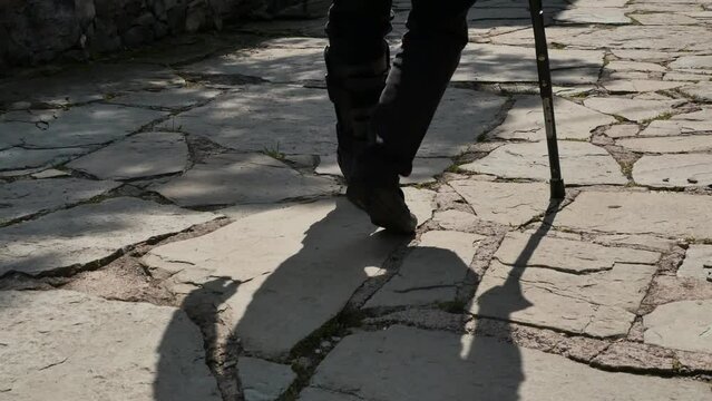 A man walks along the road leaning on a crutch and limping on his leg with a plastic corset put on it for rehabilitation after overfishing a bone in his leg.