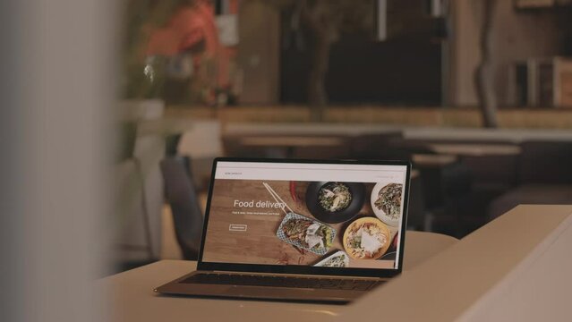 No people shot of food delivery website on laptop screen on wooden table in modern restaurant or cafe