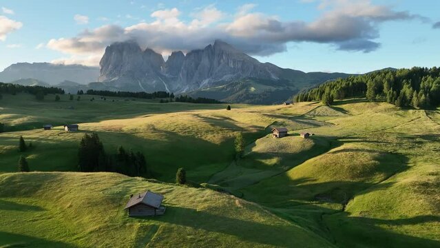 Aerial view of Seiser Alm plateau with traditional wooden mountain cottages on the meadows in Dolomites mountains in Italy . Morning drone shot of idyllic Alpe di Suisi blooming meadow in South Tyrol.