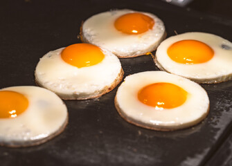 Row of fried egg on black griddle with warm lighting in a restaurant.