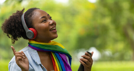 African American LGBTQ+ woman is listening to music from her smartphone while sitting relaxingly in...