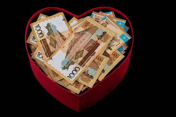 A bundle of Kazakhstani money (tenge) and a gift box in the form of a heart symbol on a black background