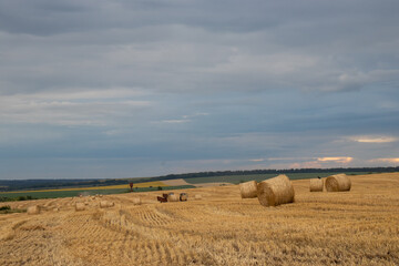 Bales of straw in the field after wheat harvesting. Summer landscape in Ukraine with straw rolls and stormy dramatic sky with clouds