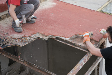 Two builders pulling the roof of a house down using a mallet.