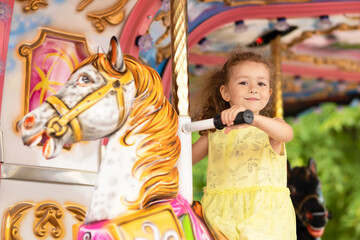 Adorable little toddler girl on carousel horse. child on attraction. kid entertainment. Happy healthy baby having fun outdoor on sunny day. Family weekend, vacations, holiday.