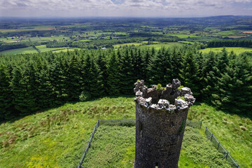 Old stone tower by a green forest in county Tipperary, close to Devil bit mountain. Ireland. Old history building preservation. Green forest and country side in the background.