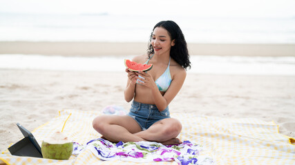 A beautiful girl sits there playing with her laptop and reading a book, and holding fruit while on vacation, a concept of traveling and vacation.