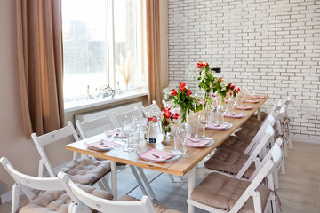 Glasses, forks, knives, napkins and a decorative flower on a dark brown wooden table served for dinner in a cozy restaurant