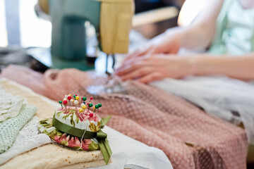 Selective focus. Close-up of a pillow for needles in the form of a hat. Against the background of women's hands in focus and sewing accessories.