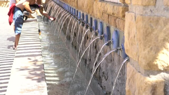 Persona irreconocible refrescando a su mascota en una fuente publica en plena ola de calor.