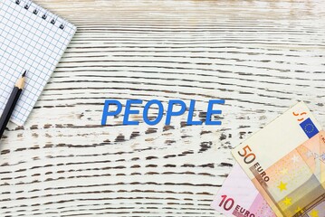 Naklejka premium PEOPLE - word (text) and euro money on a white wooden table, notebook, notepad. Business concept: buying, selling, commerce (copy space).