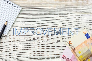 Naklejka premium IMPROVEMENT - word (text) and euro money on a white wooden table, notebook, notepad. Business concept: buying, selling, commerce (copy space).