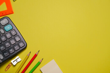 Calculator and stationery in different colors on a yellow background with copy space