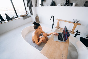 Young woman working on laptop while taking a bathtub - Powered by Adobe