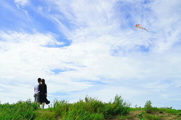 A man and a woman is watching the rainbow kite flying in blue sky.