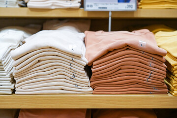 A pile of shirts, earth tone color, cream and brown was folded and put on shelf in cloth shop department store.